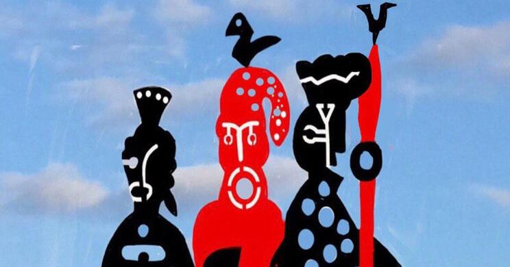Drei stilisierte, schwarz-rote Figuren mit ornamentalen Mustern stehen als Skulptur vor blauem Himmel.