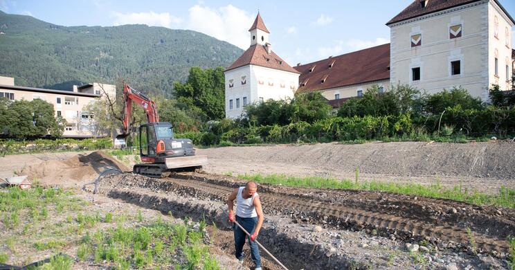 Ein Arbeiter arbeitet im Garten; im Hintergrund steht ein Bagger